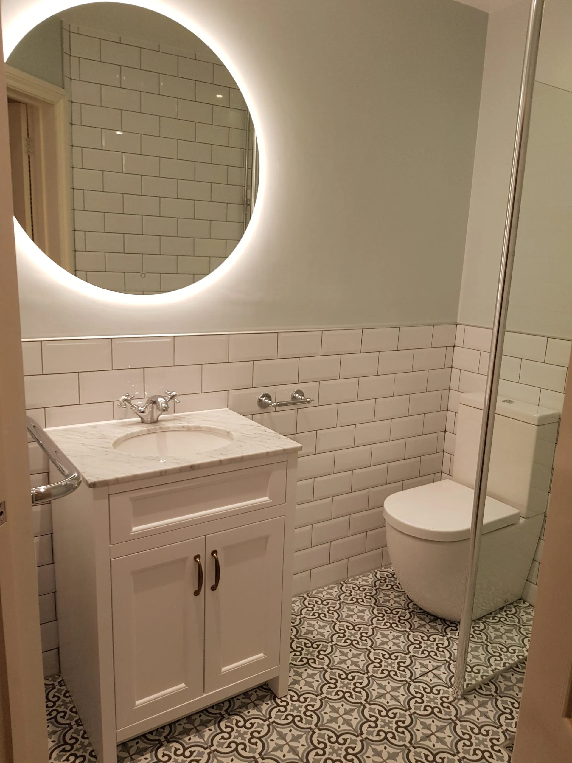 A new bathroom with a lit round mirror and a white vanity unit