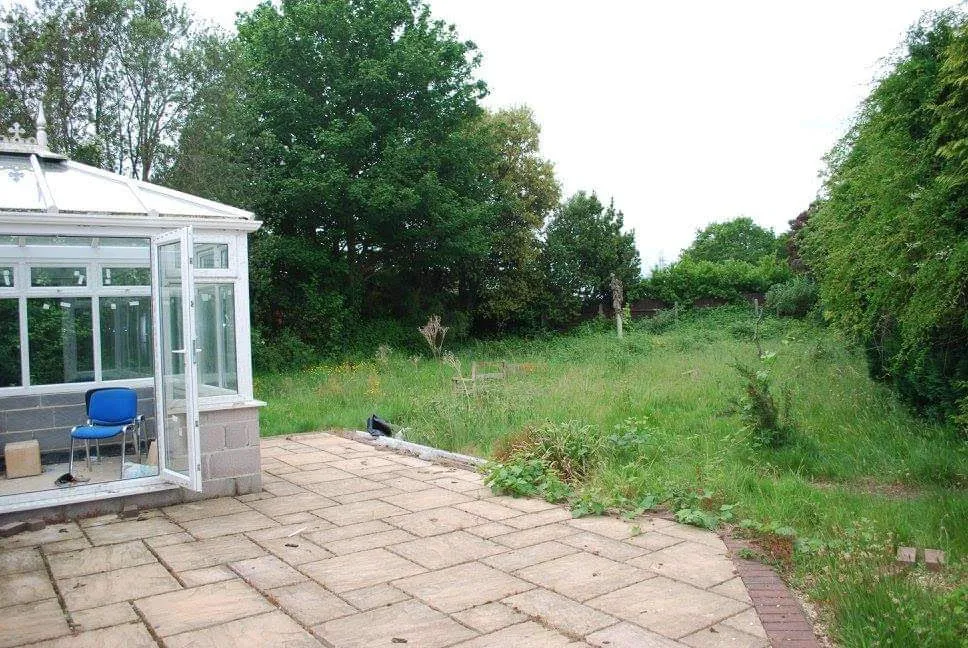 The back garden before: rough grass by the conservatory
